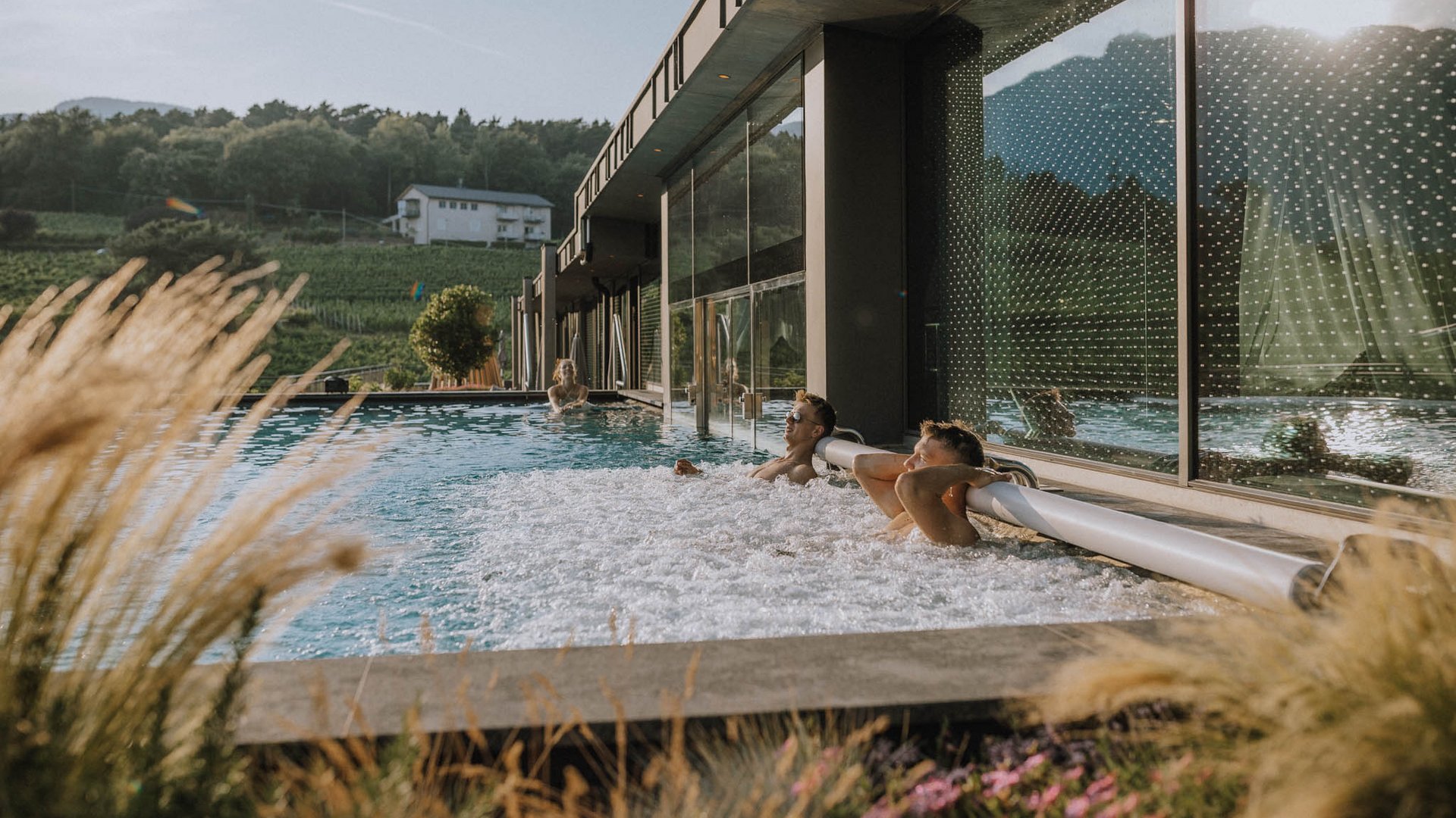 Hotel near Eppan an der Weinstraße: Gartenhotel Moser People relaxing in an outdoor pool next to a modern building with rural landscape