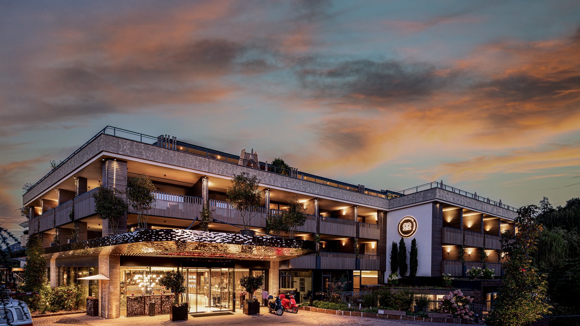 Hotels nahe dem Kalterer See 4-Sterne-Superior Modernes Hotelgebäude bei Sonnenuntergang mit beleuchtetem Eingang und Logo