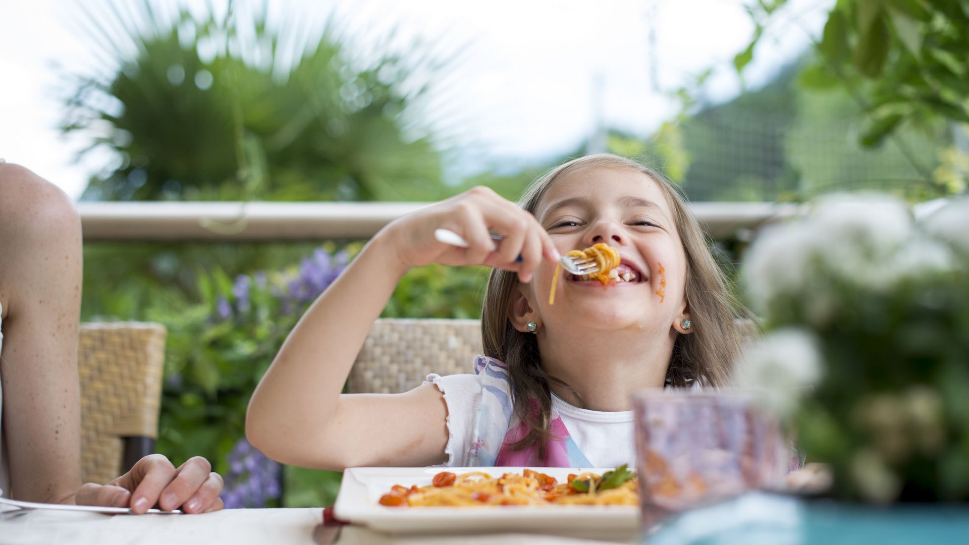 Familienhotels in Südtirol 4-Sterne-Superior Mädchen isst lachend Spaghetti im Freien