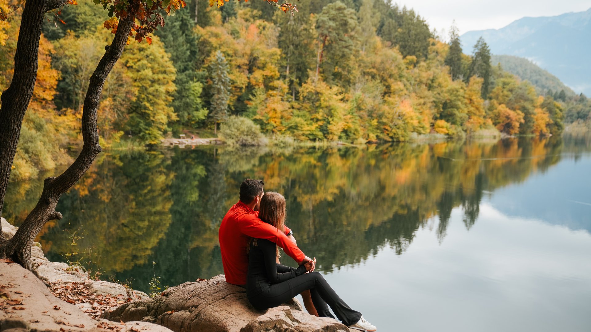 Hotels nahe dem Kalterer See 4-Sterne-Superior Ein Paar sitzt an einem ruhigen See im herbstlichen Wald