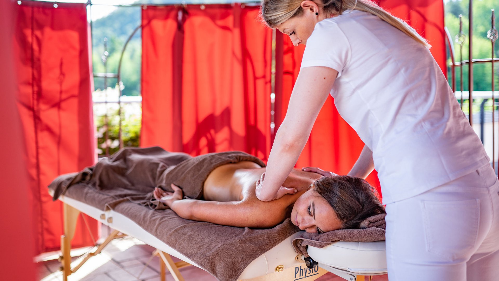 Hotel on Lago di Monticolo/Montiggler See: Gartenhotel Moser Woman getting a massage on a table in a relaxing area with red curtains