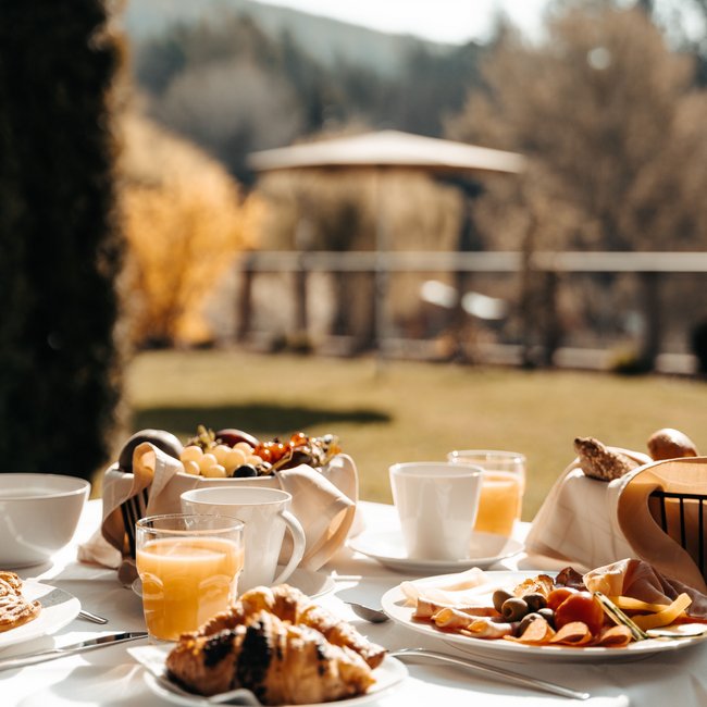 Gourmethotel in Südtirol: Gartenhotel Moser Frühstückstisch mit Croissants, Saft und Obst im Garten an sonnigem Tag