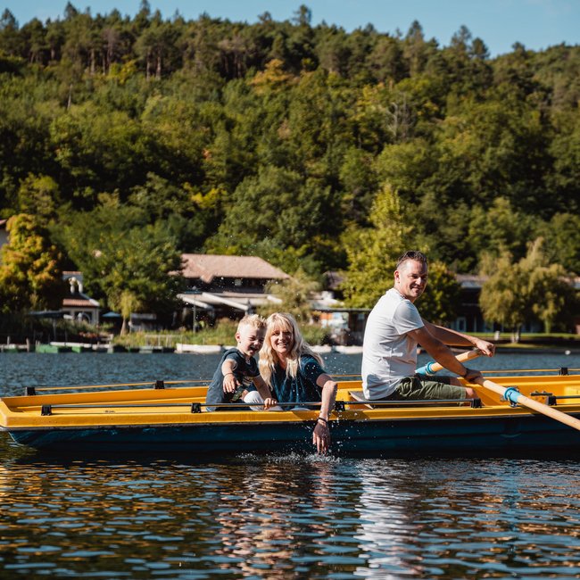 Wellnessurlaub am See: Gartenhotel Moser Familie fährt mit einem gelben Ruderboot auf einem See bei sonnigem Wetter