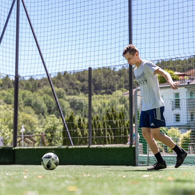 Familienhotels in Südtirol 4-Sterne-Superior Junger Mann spielt Fußball auf einem Außenplatz mit Tor und Netz