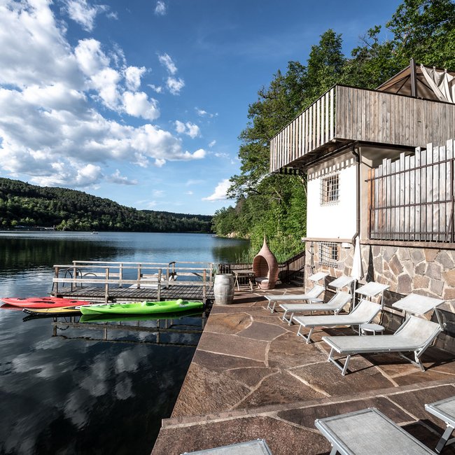 Hotel on Lago di Monticolo/Montiggler See: Gartenhotel Moser Lake view with sun terrace and kayaks on the dock under cloudy sky