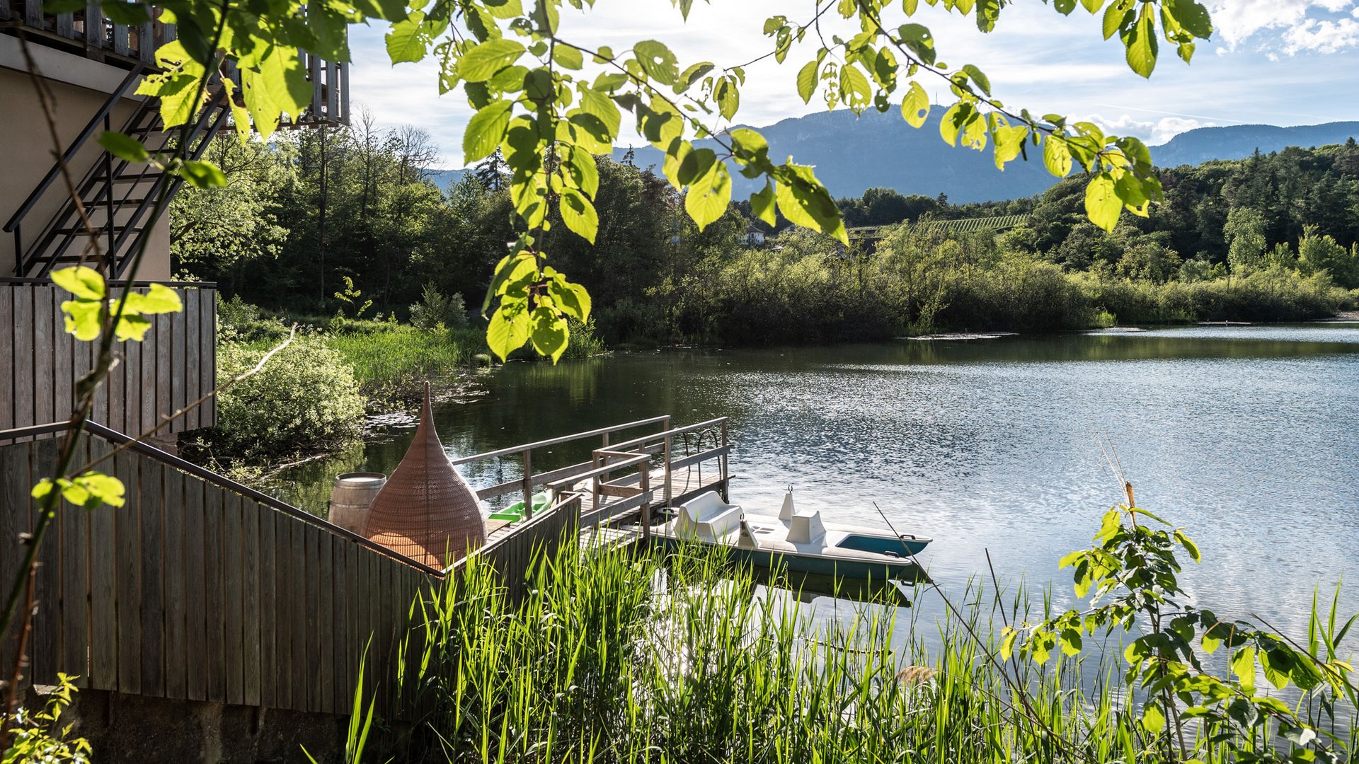 Wellnessurlaub am See: Gartenhotel Moser Sonnenlicht durch grüne Blätter an einem See mit Steg und Ruderboot