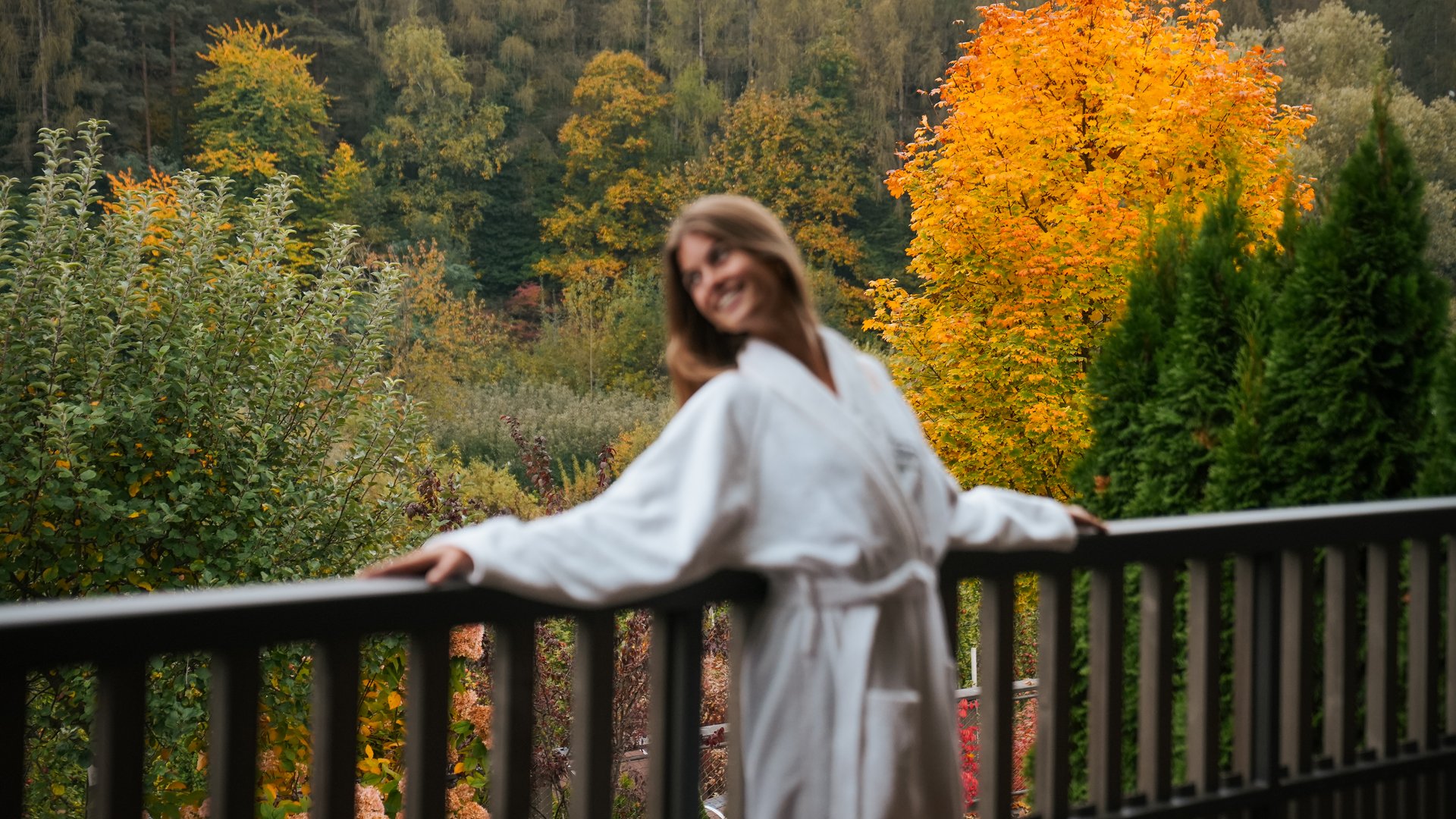 Hotels nahe dem Kalterer See 4-Sterne-Superior Frau im weißen Bademantel auf Balkon mit herbstlichem Farbenspiel