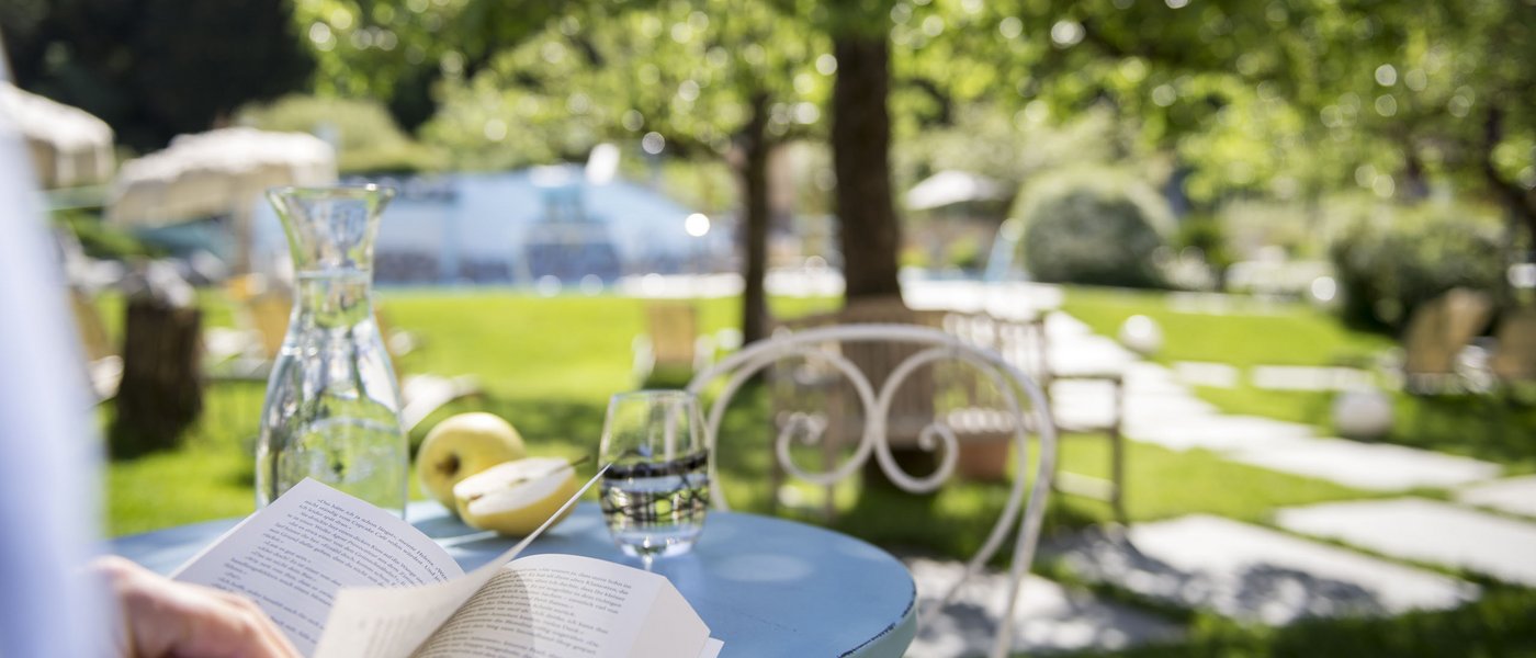 Hotel near Eppan an der Weinstraße: Gartenhotel Moser Person reading book in garden with water jug and apple on blue table
