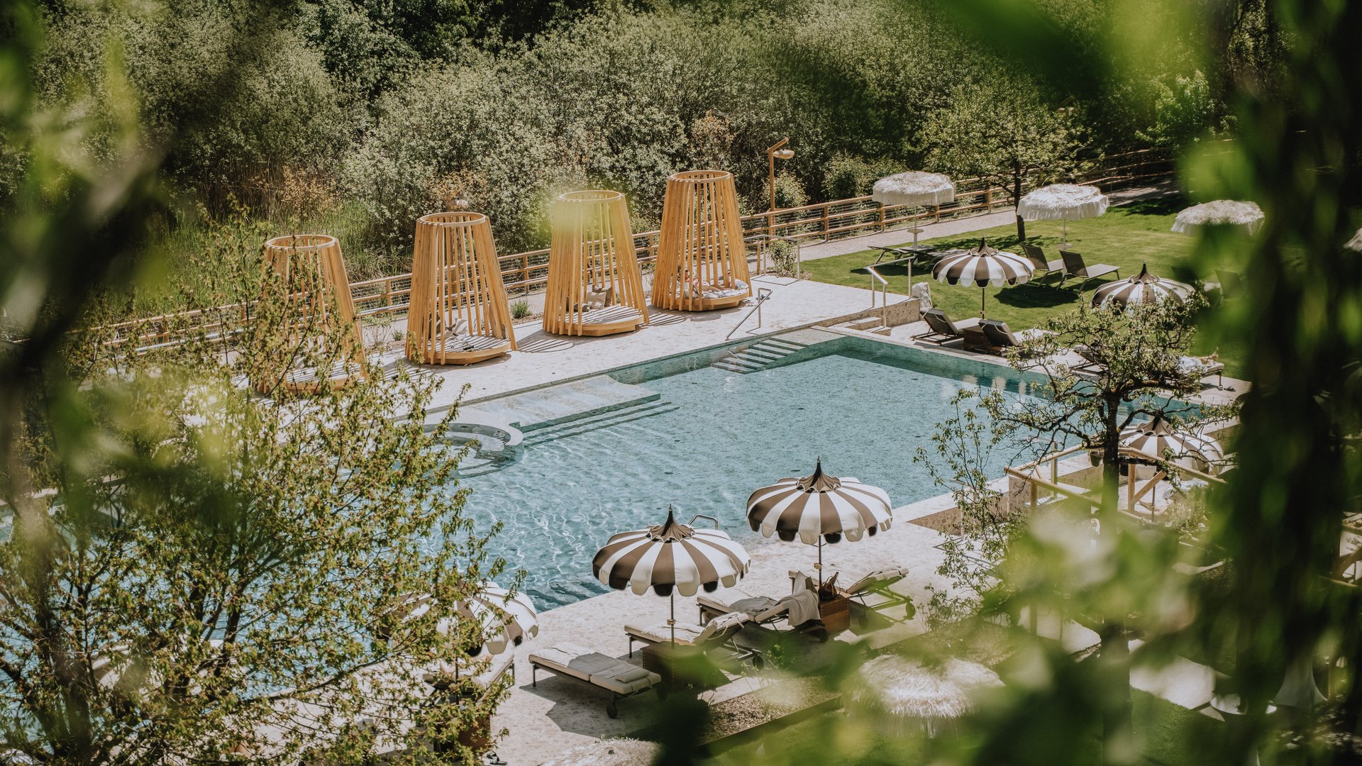 Hotels nahe dem Kalterer See 4-Sterne-Superior Blick auf einen Pool mit Liegestühlen und Sonnenschirmen in einer grünen Umgebung